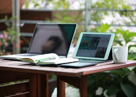A cozy outdoor workspace scene with a laptop, tablet, and mug on a wooden table.